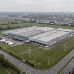 Quels data centers près de chez vous choisir pour un cloud plus sobre ? Vue aérienne réaliste d’un centre de données régional français entouré de lignes électriques, d’infrastructures de fibre optique et d’un paysage urbain sobre.